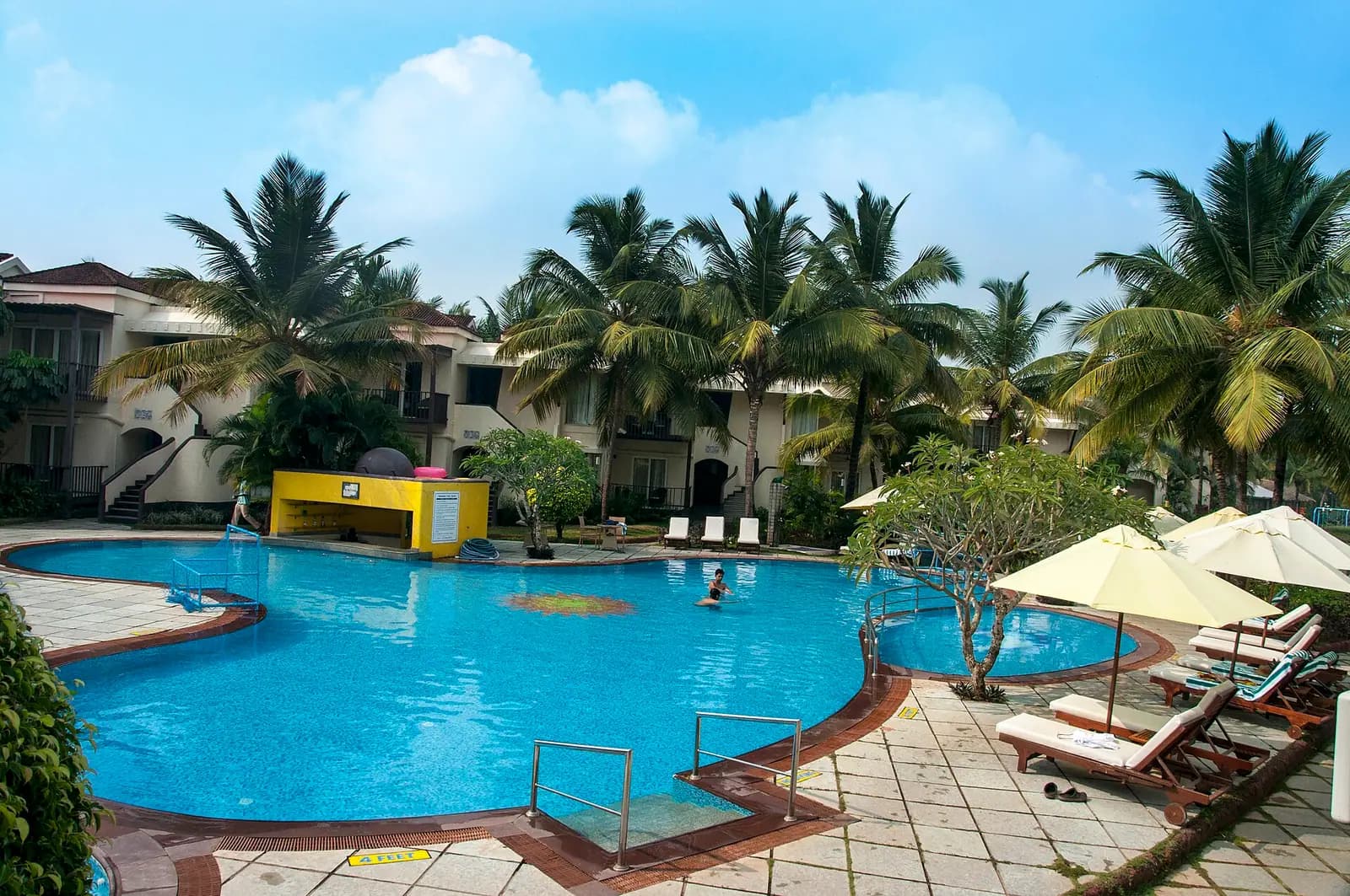 A beachfront resort pool shaded by palms in Goa