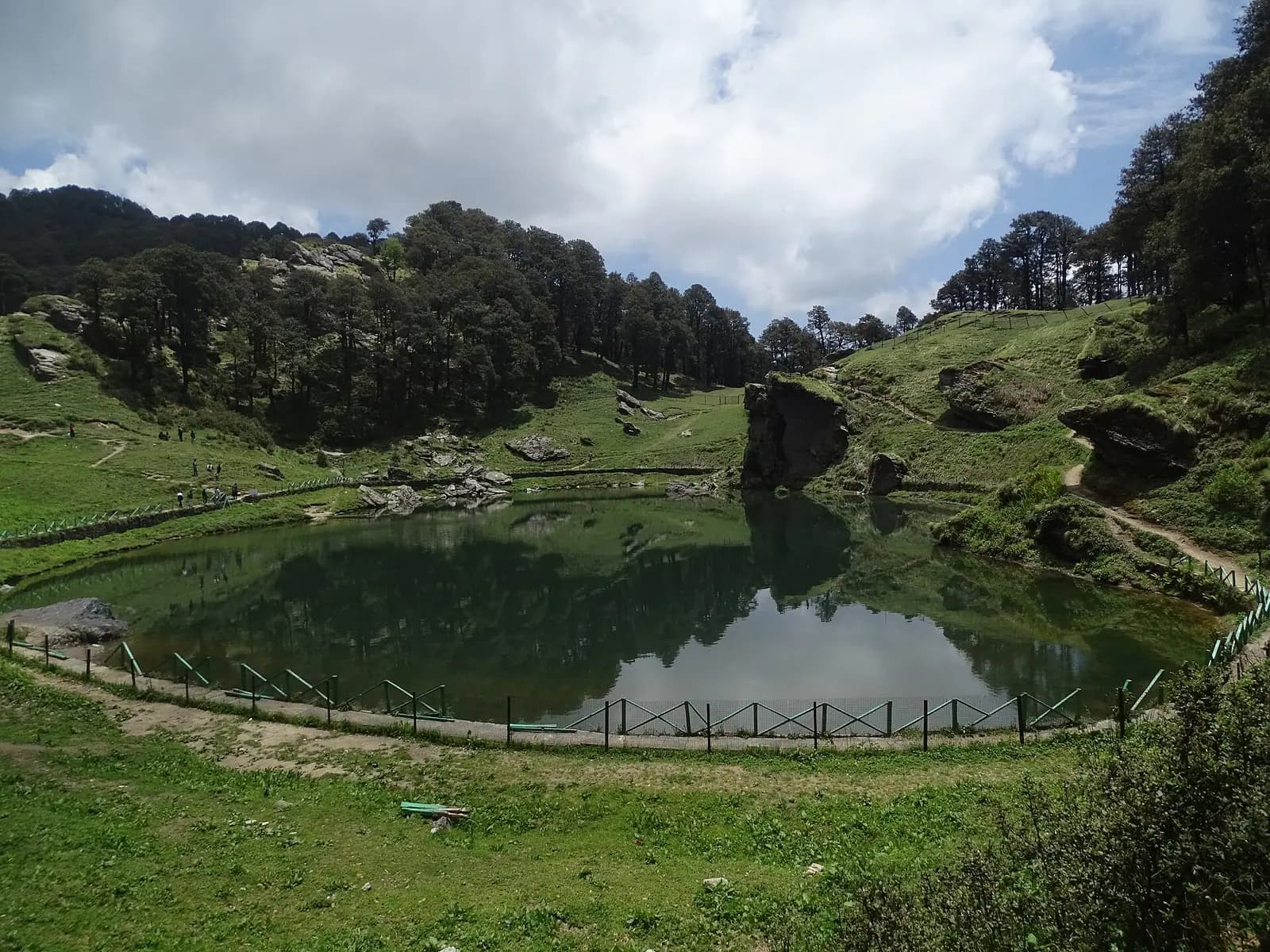 The still water of Serolsar Lake ringed by old forest above Jalori Pass